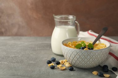 Müsli, süt ve yaban mersinli kahvaltı fikri gri masada.