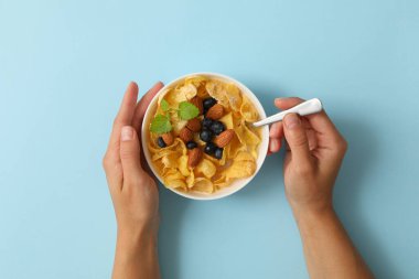 Kadın eli mavi arka planda bir kase müsli tutuyor.
