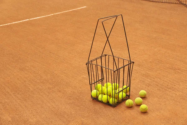 Basket with tennis balls on clay court, space for text