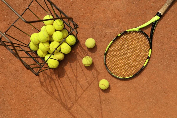 Racket and basket with tennis balls on clay court