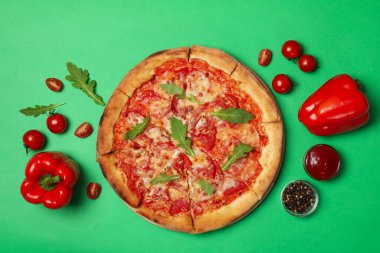 Lezzetli pizza ve yeşil arka planda malzemeler.