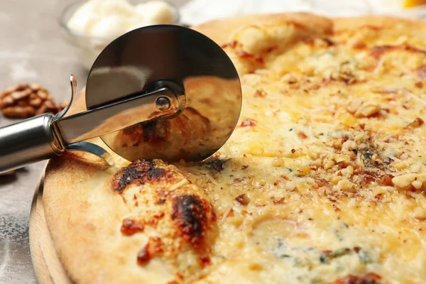 Pizza cutter and cheese pizza, close up