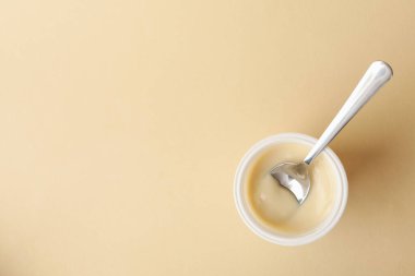 Bej arka planda kaşık olan plastik bir bardak yoğurt.