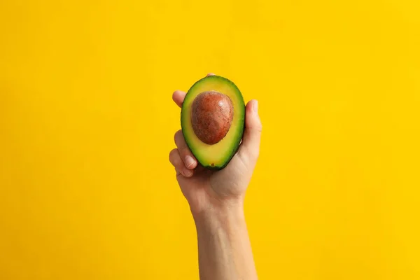 Vrouwelijke Hand Houden Avocado Gele Achtergrond — Stockfoto