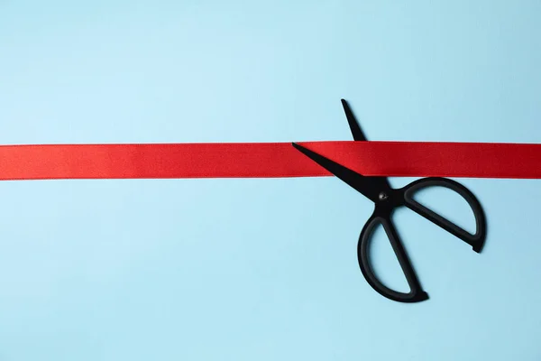 Black scissors and red ribbon on blue background