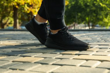 Siyah spor ayakkabılı ve eşofmanlı adam parkta koşuyor.