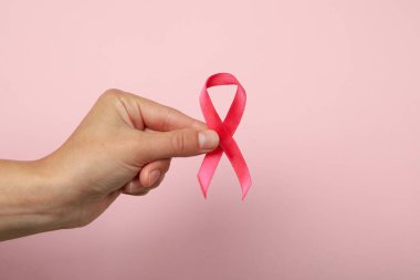 Pembe arka planda pembe farkındalık kurdelesi olan bir kadın el.