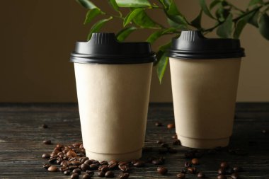 Kağıt bardaklar, kahve çekirdekleri ve ahşap arka planda bitki.