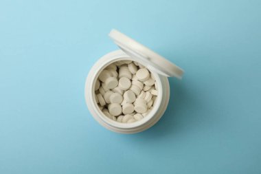 Mavi arka planda hapları olan ilaç şişesi.