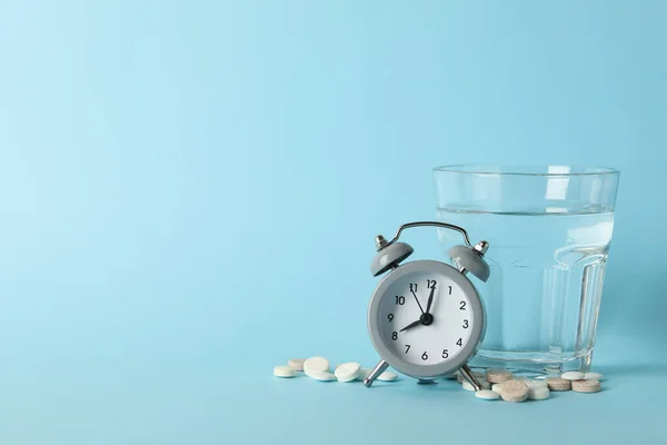 Glass of water, alarm clock and pills on blue background