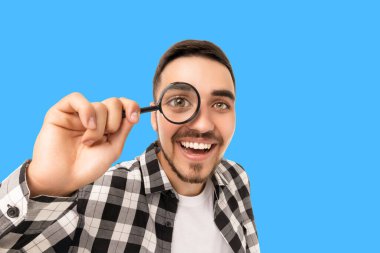 Gülümseyen genç adam elinde büyüteçle merakını dile getiriyor.