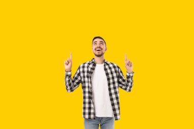 Neşeli genç adam gülümseyerek yukarısındaki bir şeyi işaret ediyor.