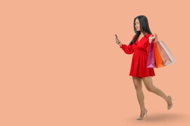 Genç bir kadın alışveriş poşetleri taşırken online alışveriş yapmaktan hoşlanıyor