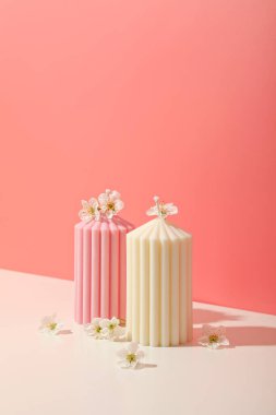 İki renkli mum küçük çiçeklerle süslenmiş pastel bir yüzeye oturur.