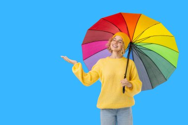 Sarı kazaklı kadın açık gökyüzünde parlak bir şemsiye tutuyor