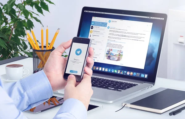 Telegram messenger op de iphone-scherm in mannelijke handen en desktop-versie van de Telegram op macbook — Stockfoto