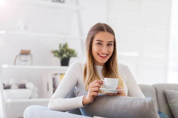 一杯のコーヒーとソファの上に座っている若い女性の肖像画 — ストック写真