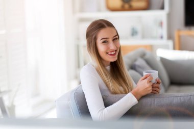 Kahve ile kanepede oturan genç bir kadın portresi