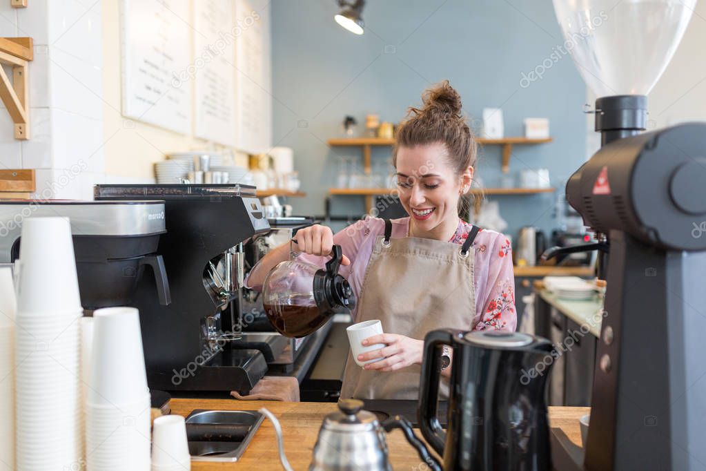 Young barista preparing coffee for customers at her cafe counter