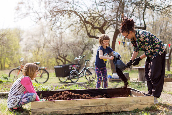 Mother with two young daughters gardening in urban community garden