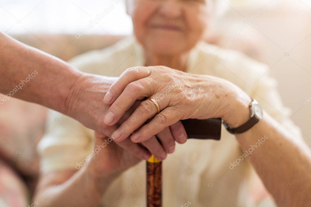 Close-up of woman holding senior's hands leaning on walking cane