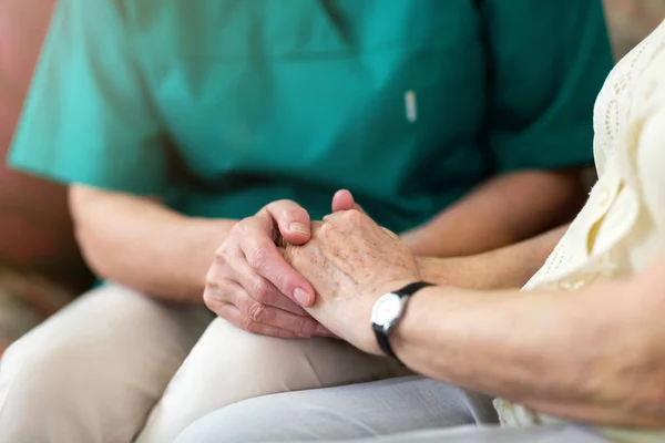 Nurse consoling her elderly patient by holding her hands