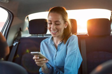 Arabanın arka koltuğunda akıllı telefonu olan genç bir kadın.