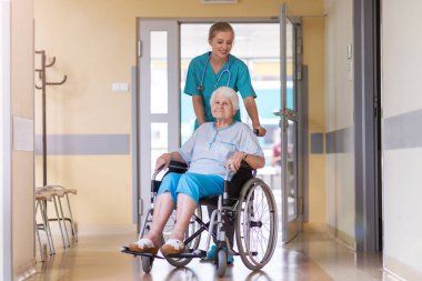 Senior woman in wheelchair with nurse in hospital clipart