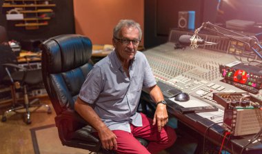 Çok kanallı bir konsolda oturan bir kayıt stüdyosunda erkek orta yaşlı kayıt mühendisi