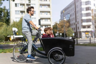 Baba ve çocuklar bir şehirde kargo bisikleti ile bir yolculuk sahip