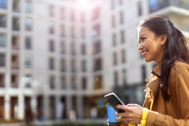 Şehirde akıllı telefon ve kahve ile genç kadın 