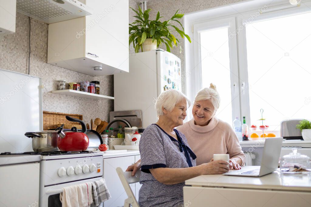 Adult daughter teaching her elderly mother to use laptop