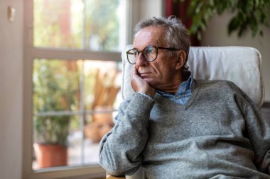 Senior man looking out of window at home clipart