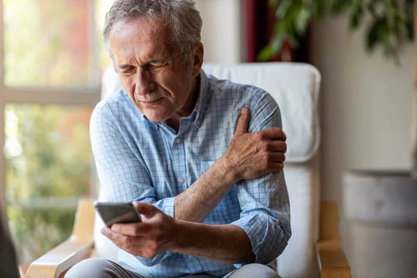老年人在家里用智能手机时感到疼痛 — 图库照片