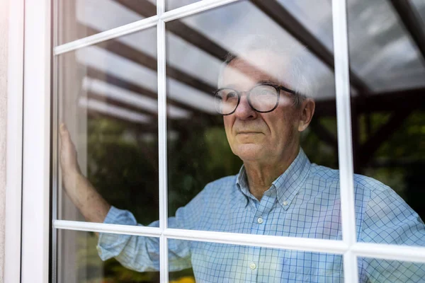 Senior Man Die Thuis Uit Het Raam Kijkt Stockfoto