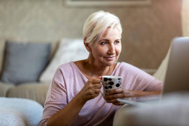 Evde laptop kullanan olgun bir kadın.