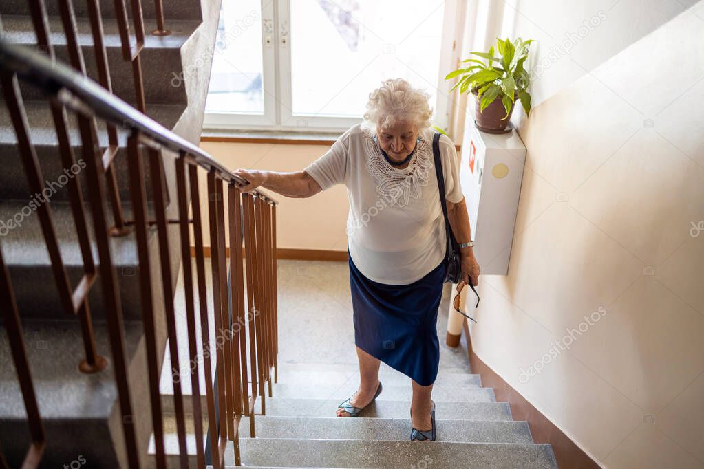 Senior woman climbing staircase with difficulty 
