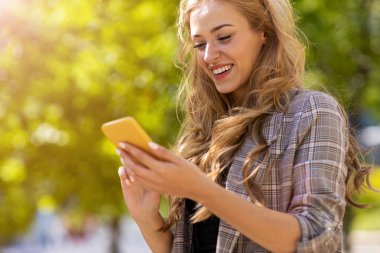 Şehirde akıllı telefon kullanan mutlu genç bir kadın.