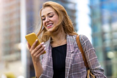 Şehirde akıllı telefon kullanan mutlu genç bir kadın.