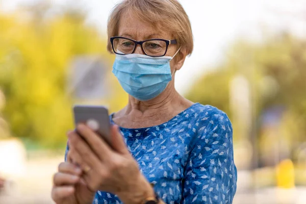 Ηλικιωμένη Γυναίκα Που Χρησιμοποιεί Smartphone Φορώντας Προστατευτική Μάσκα Προσώπου — Φωτογραφία Αρχείου