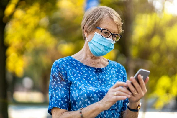 Senior Kvinna Som Använder Smartphone Medan Bär Skyddande Ansiktsmask — Stockfoto