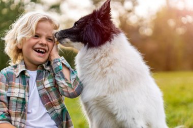 Küçük çocuk parkta köpeğiyle oynuyor.