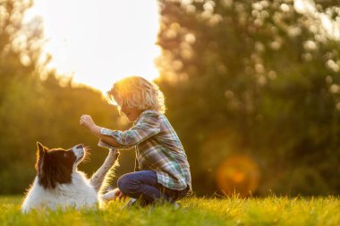Küçük çocuk parkta köpeğiyle oynuyor.