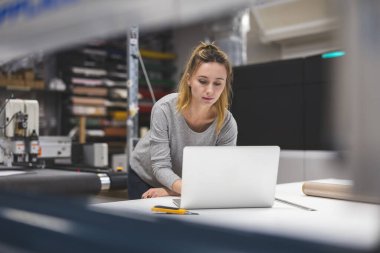 Matbaada dizüstü bilgisayar kullanan bir kadın.