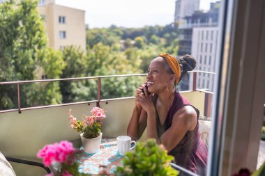 Woman drinking coffee and using mobile phone at home balcony