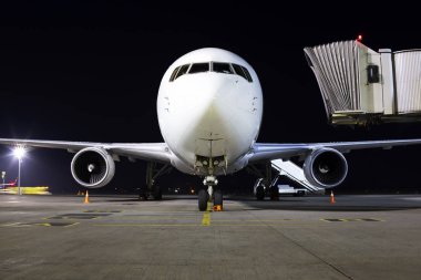 Büyük, modern, beyaz bir uçak havaalanının otoparkında gece görüş alanında.