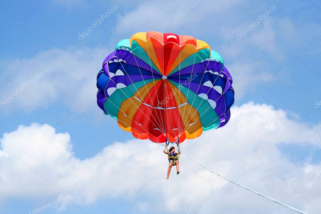 tiny happy girl on colorful parasail in the blue sky