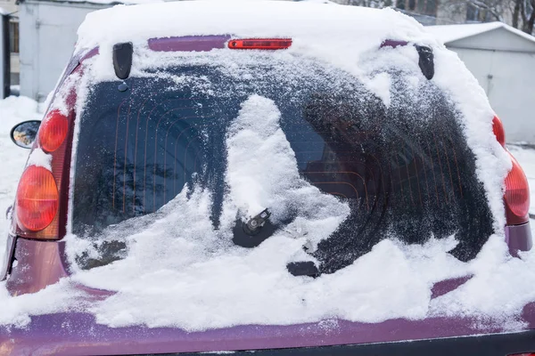 The car, covered with thick layer of snow. Negative consequence of heavy snowfalls. Close-up shot of a car's windscreen wiper covered in snow