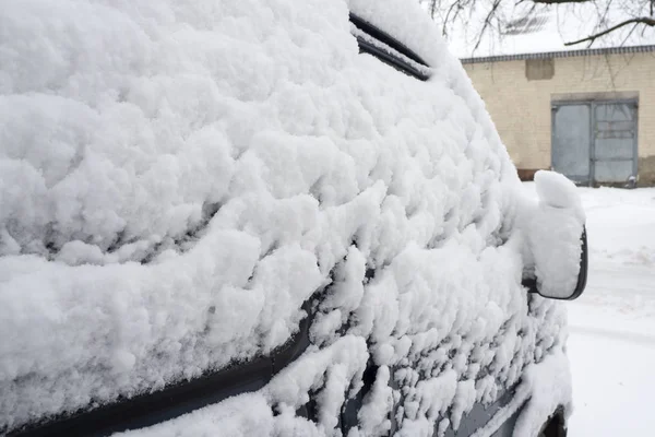 Courtyard after heavy snowfall. The car, covered with thick layer of snow. Right side of a luxury car covered with snow