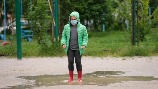 Una Niña Con Una Máscara Médica Botas Goma Salta Través — Vídeos de Stock